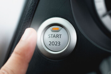 Finger about to press a car ignition button with the text 2023 start. Year two thousand and twenty...