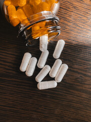 Glass jar of pills scattered on surface of wooden table, vertical photo. Tablets in capsules,...