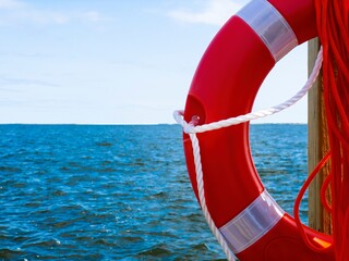 Half of an orange ring buoy life preserver in selective focus, with orange rope, hanging at a...