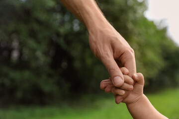 Daughter holding father's hand in park, closeup. Happy family