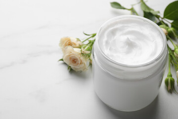 Jar of hand cream and roses on white marble table, space for text