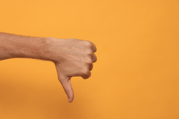 Man showing thumb down on orange background, closeup. Space for text