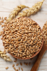 Wheat grains in bowl on white wooden table, top view