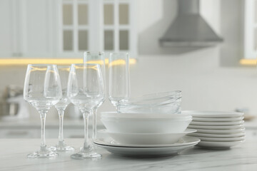 Fototapeta na wymiar Different clean dishware and glasses on white marble table in kitchen