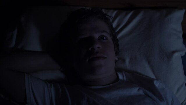 A young high school aged teenager lays in his bed at night looking sad and serious.

- teen boy, teenager, sad, depressed, troubled, alone, lonely, young man