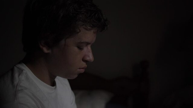 A young high school aged teen boy looking sad and depressed and serious sitting on his bed at night.

- teen boy, teenager, sad, walking, depressed, troubled, alone, lonely, young man, walking