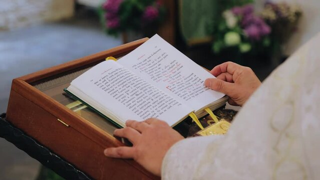 The priest stands in front of the bible and reads a prayer. The book lies on a pedestal in front of the priest
