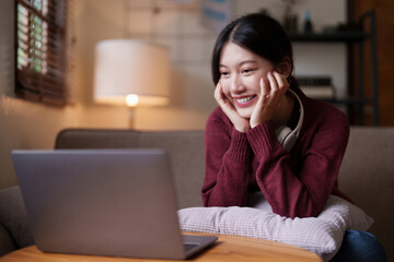 Young asian woman sitting on couch looking at laptop in cozy living room at home. Lifestyle concept
