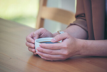 Close up Woman hand holding black coffee cup in green garden cafe. Hands of businesswoman love drinking hot coffee. business women with black coffee or hot chocolate in coffee shop. Caffeine drinking