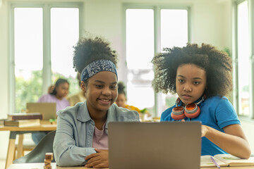 Two young African girls use computer notebook for an online class with support from a teacher. Kids use technology for a distance education program in a class