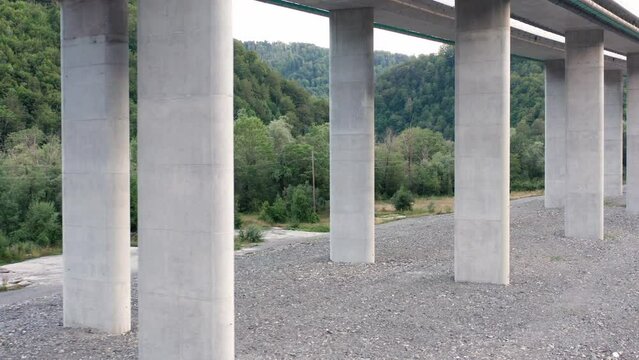 Reinforced concrete pillars supporting a bridge on a highway. Columns under a viaduct or overpass (elevated road) - supporting traffic lanes. Transport and its impact on the green forest environment.