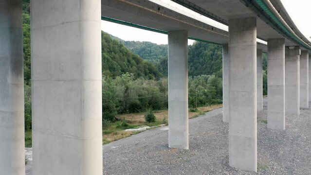 Reinforced concrete pillars supporting a bridge on a highway. Columns under a viaduct or overpass (elevated road) - supporting traffic lanes. Transport and its impact on the green forest environment.