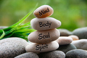 Mind, Body, Soul and Spirit words engraved on zen stones with blurred nature background. Copy space...