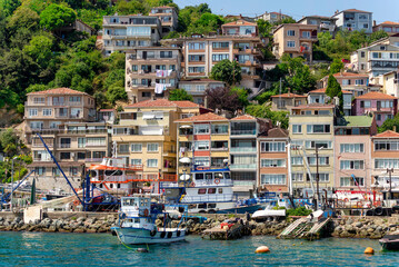 Fototapeta na wymiar View from the sea of the green mountains of the Europian side of Bosphorus strait, with docked boats, traditional houses and dense trees in a summer day