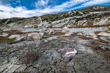 Drying soil cracks, stones and coastal hills under blue sky with white clouds
