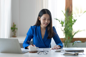 Asian businesswoman sitting happily with her laptop and takes notes intensely and smiles happily at her assignment.
