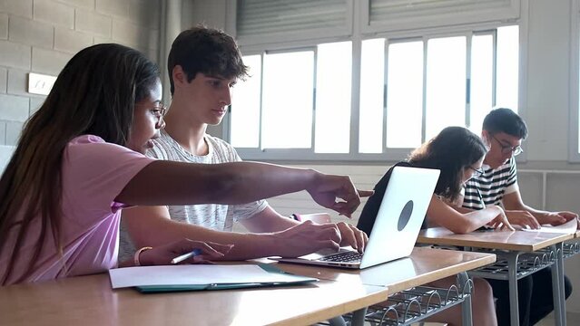 Black teen girl high school student and white teenage boy talk in class doing homework using laptop.Handheld 4k video.