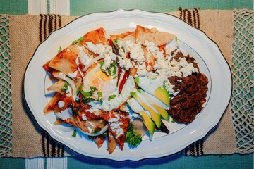 Chilaquiles Mexican food with in red sauce, cheese, cream and chili peppers on vintage background