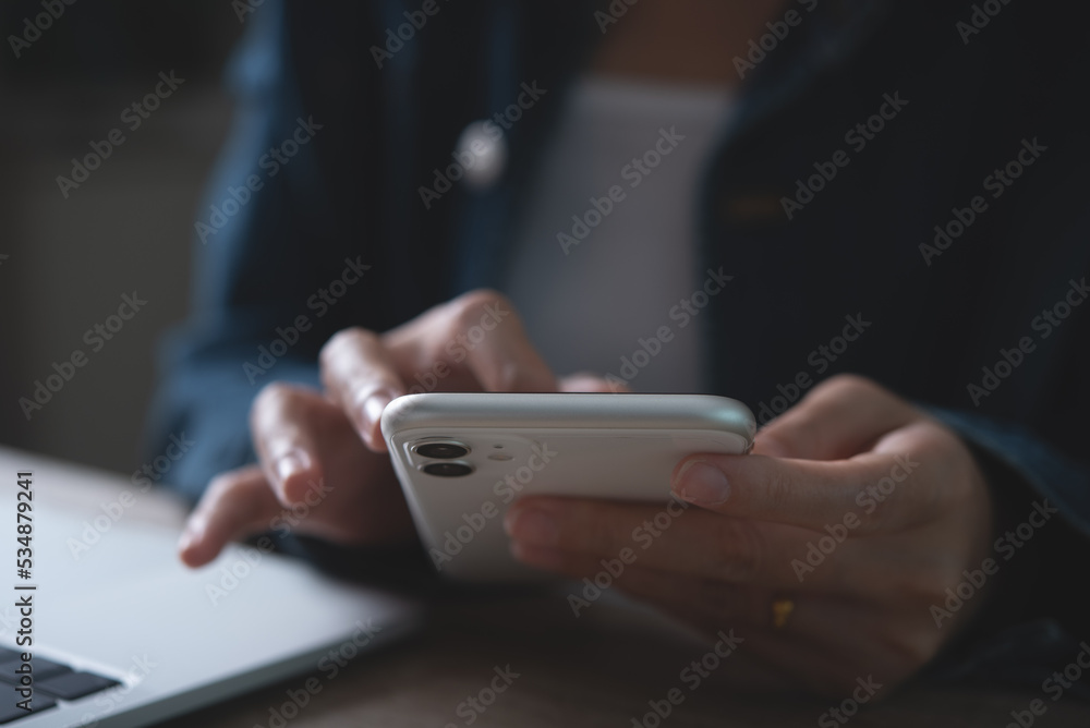 Poster closeup of business woman using mobile smart phone and working on laptop computer with digital table