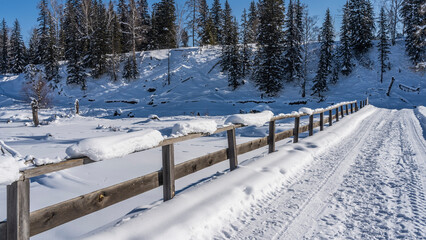 An old bridge over a frozen river. Tire tracks are trampled in the snow. There is a layer of snow...