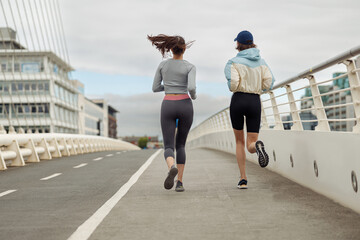 Two athletic women in sportswear is jogging on a bridge. Reaching the goal. Back view