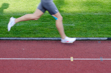 Runner legs with white spikes in motion on the red track.