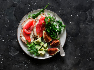 Fototapeta na wymiar Delicious breakfast, snack, appetizer - salmon sandwich, avocado, arugula, figs on a dark background, top view