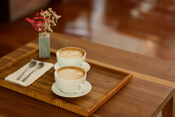 2 cups of hot latte coffee, put on a cutting board, put flowers together Placed at a coffee shop, Chiang Mai, Thailand on 29.92.2022.