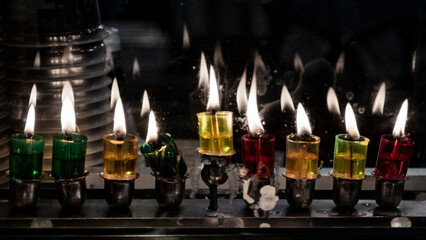 Multi-colored glass vials hold oil and burning wicks in a menorah glowing brightly on the eighth night of the Jewish festival of Hanukkah.
