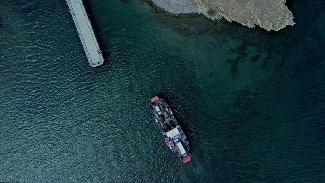 4k Top view of ship with cargo moves through water and comes to port irrl. Aerial picture of large vehicle with cars on top moving on sea and delivering goods, mooring to shore in open air. Operator