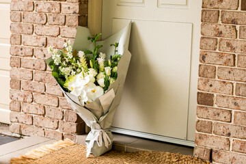 A bouquet of flowers delivered on a porch doorsteps of a house front door. Surprise contactless delivery. Mother's Day, Valentine's Day, Birthday, Celebration and Anniversary concept