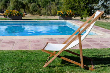 White wooden deck chair, on grass and in front of a swimming pool.