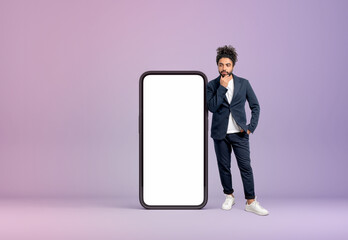 Middle eastern man hand to chin near phone, mockup display on lilac background