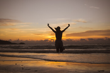 Silhouette of happy joyful woman jumping at the beach against the sunset. Freedom life vacation concept