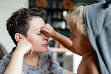 mother and child use cosmetics together. A little daughter paints her mother's eyes with glittery shadows.