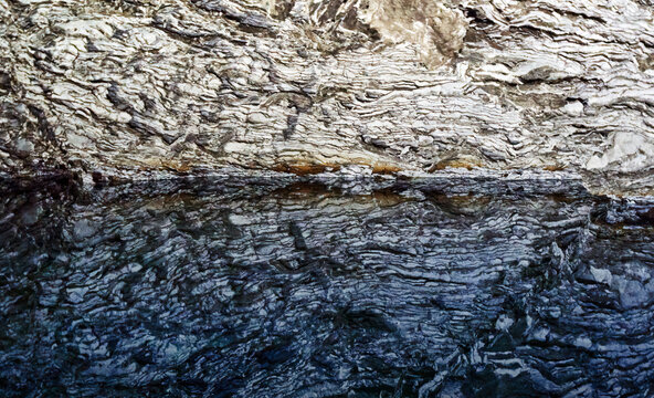 Reflection of anhydrite banded by clay deposits in the water of a subterranean groundwater lake in a cave