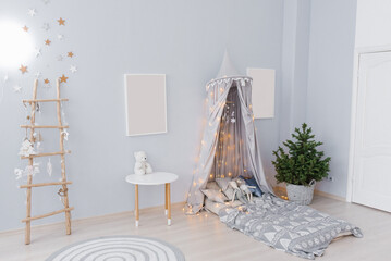 Cute Christmas baby room decor in blue colors. A bed with an awning, a tree in a pot, mockups of a picture on the wall