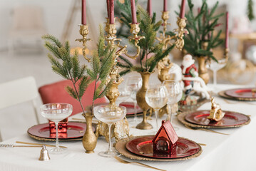 Christmas serving of a festive New Year's dinner. Candles in candlesticks, spruce branches, red and gold plates