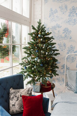 Christmas tree in the bedroom by the window, decorated for Christmas. Cozy interior of a house or apartment