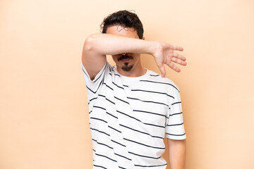 Young caucasian man isolated on beige background covering eyes by hands