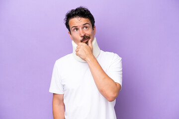 Young caucasian man wearing neck brace isolated on purple background having doubts