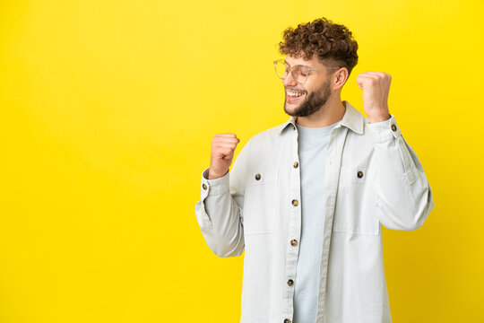 Young handsome caucasian man isolated on yellow background celebrating a victory