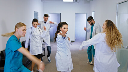 Happy and excited doctors and nurses with a large smile dancing in front of the camera in a modern hospital corridor