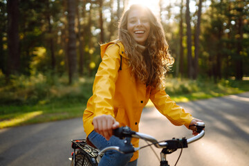 Beautiful happy woman in yellow coat riding bicycle in autumn park. Autumn fashion. Lifestyle....