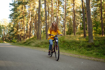 Beautiful happy woman in yellow coat riding bicycle in autumn park. Autumn fashion. Lifestyle. Relax, nature concept.