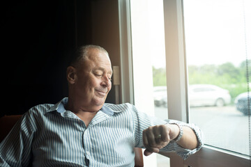 Businessman 60s checking watch sitting by window 
