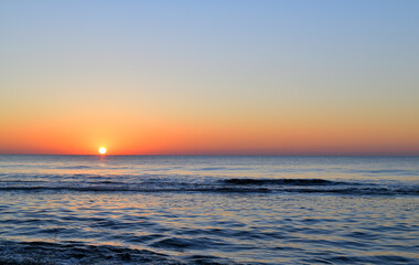 Das Blaue Meer in der Abenddämmerung und die Sonne geht am Horizont mit roten Farben. unter.