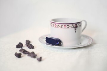 Tasse de thé violette et blanche avec des violettes cristallisées et un bonbon à la violette sur fond blanc style classique - obrazy, fototapety, plakaty