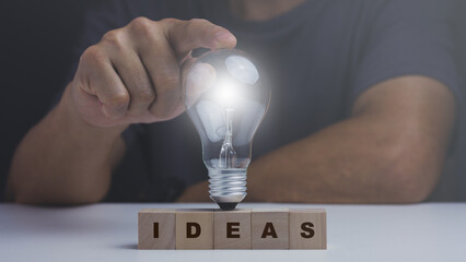 Ideas concept, man point light bulb on wood block letter, inspiration innovation.