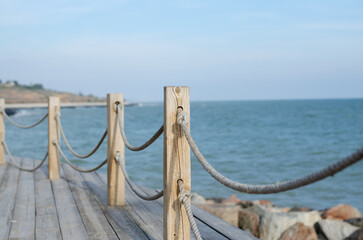 Fototapeta premium Wooden platform on the seashore. Fence made of old marine rope. Rope knot. Wooden poles. Yacht mooring.